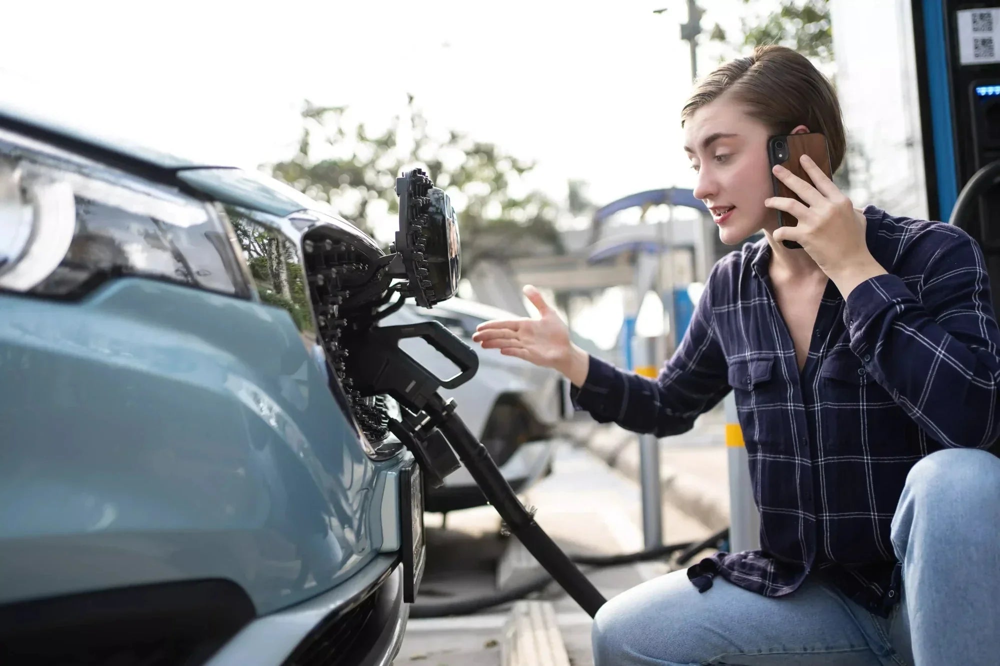 Woman on phone at EV charging station with electric car charging problem
